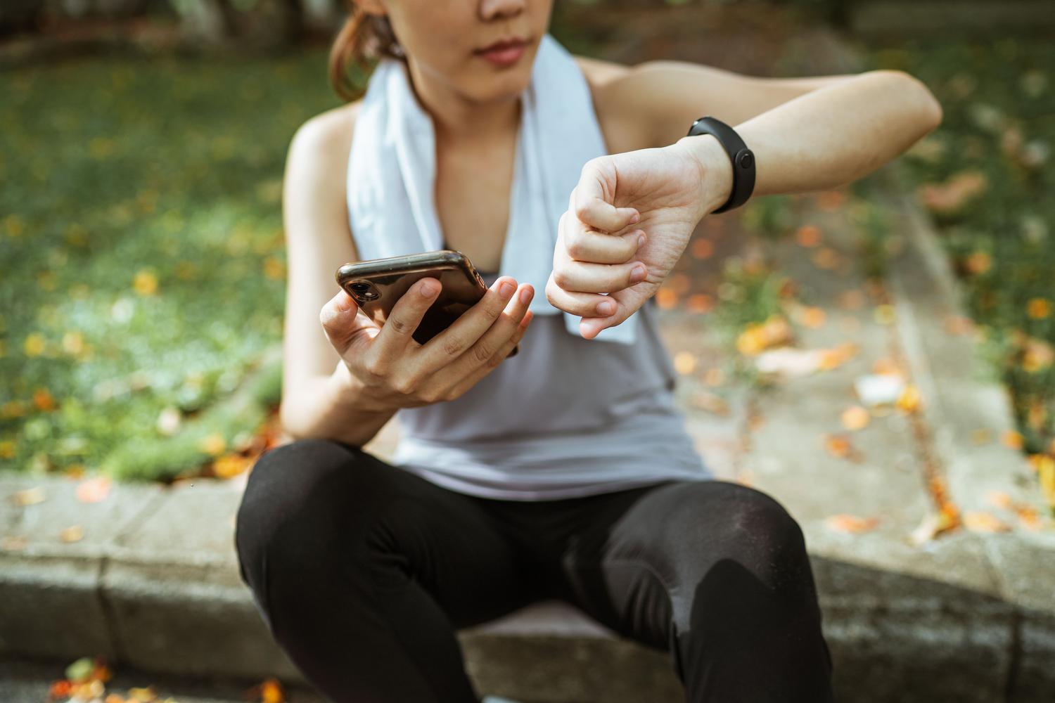 Mujer deportista utilizando simultáneamente su smartphone y smartwatch después de entrenar para revisar sus métricas.