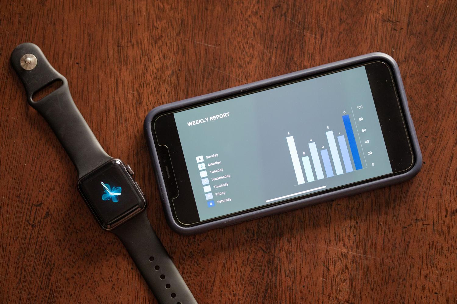 Sincronización de datos entre un smartwatch y un smartphone sobre una mesa de madera, mostrando un reporte de actividad semanal.