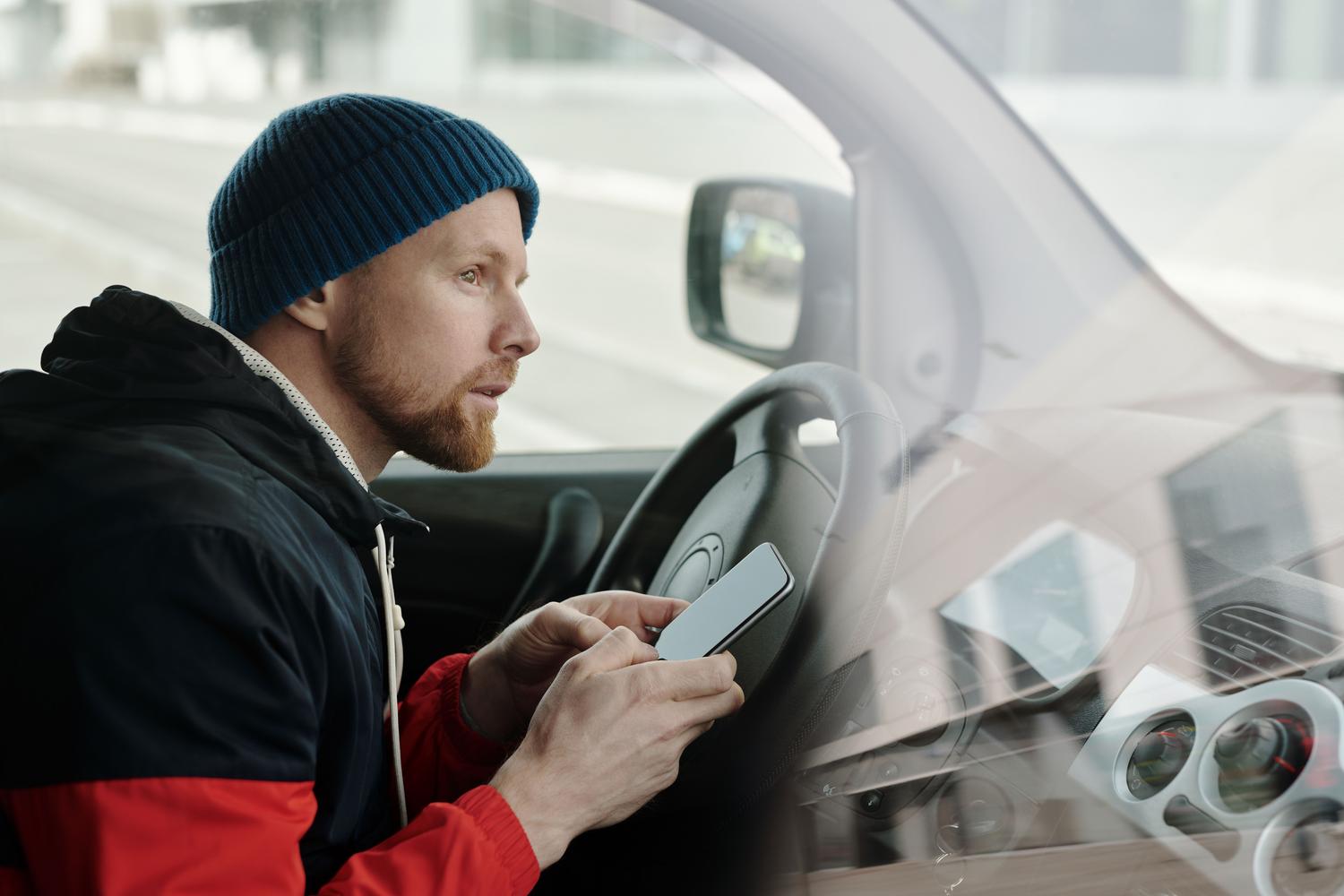 Hombre consultando su teléfono móvil en el interior de un coche aparcado para revisar su carnet digital