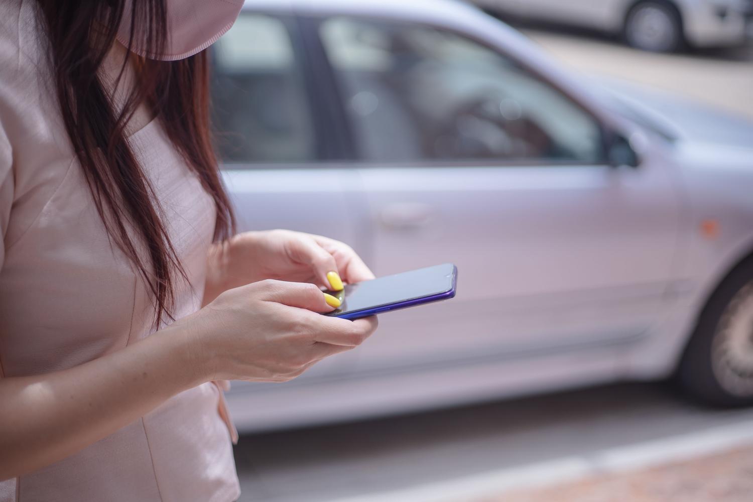 Mujer utilizando un smartphone junto a un coche aparcado al aire libre.