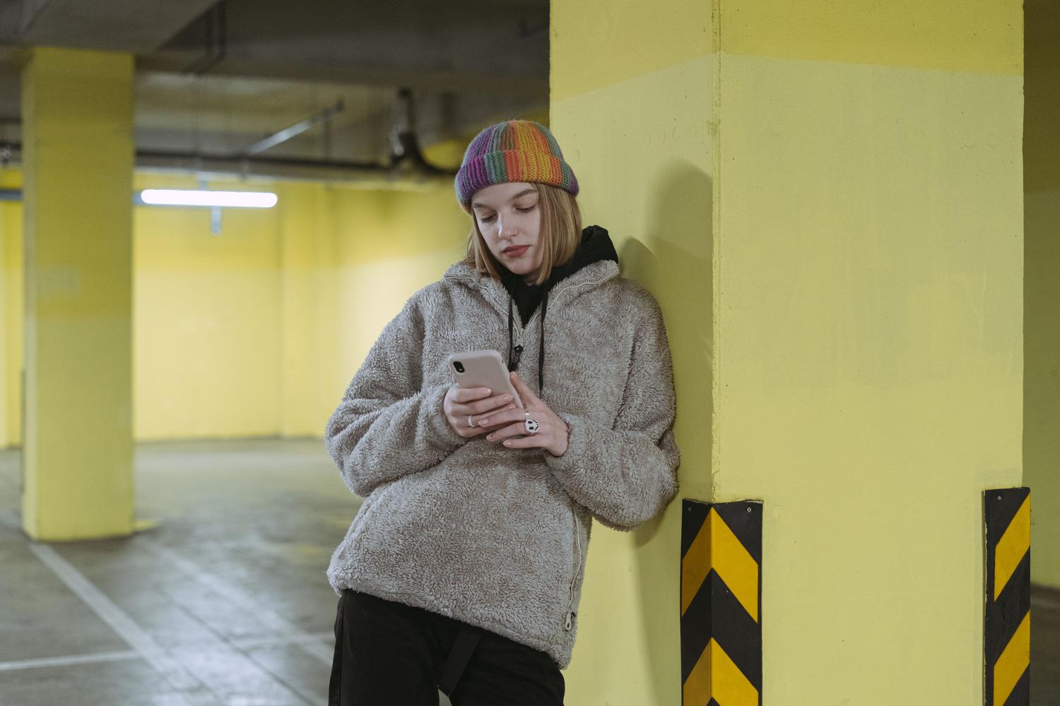 Mujer usando su teléfono móvil junto a una columna amarilla en un parking interior para guardar la ubicación de su coche.