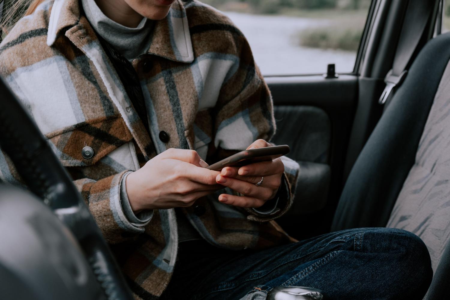 Persona sentada en el interior de un vehículo utilizando un teléfono inteligente.