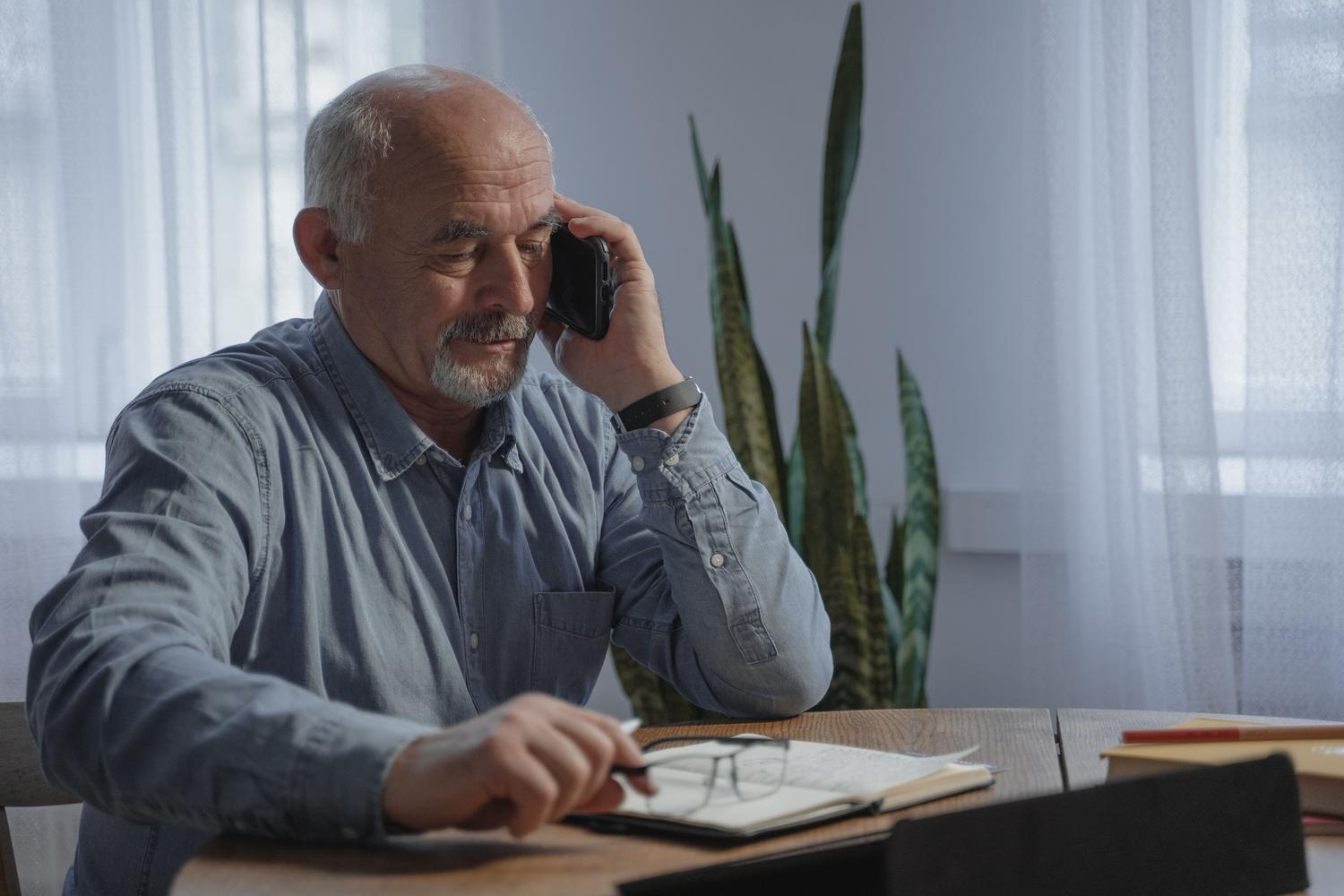 Hombre mayor realizando una llamada telefónica desde su oficina en casa, donde la señal celular suele ser débil.
