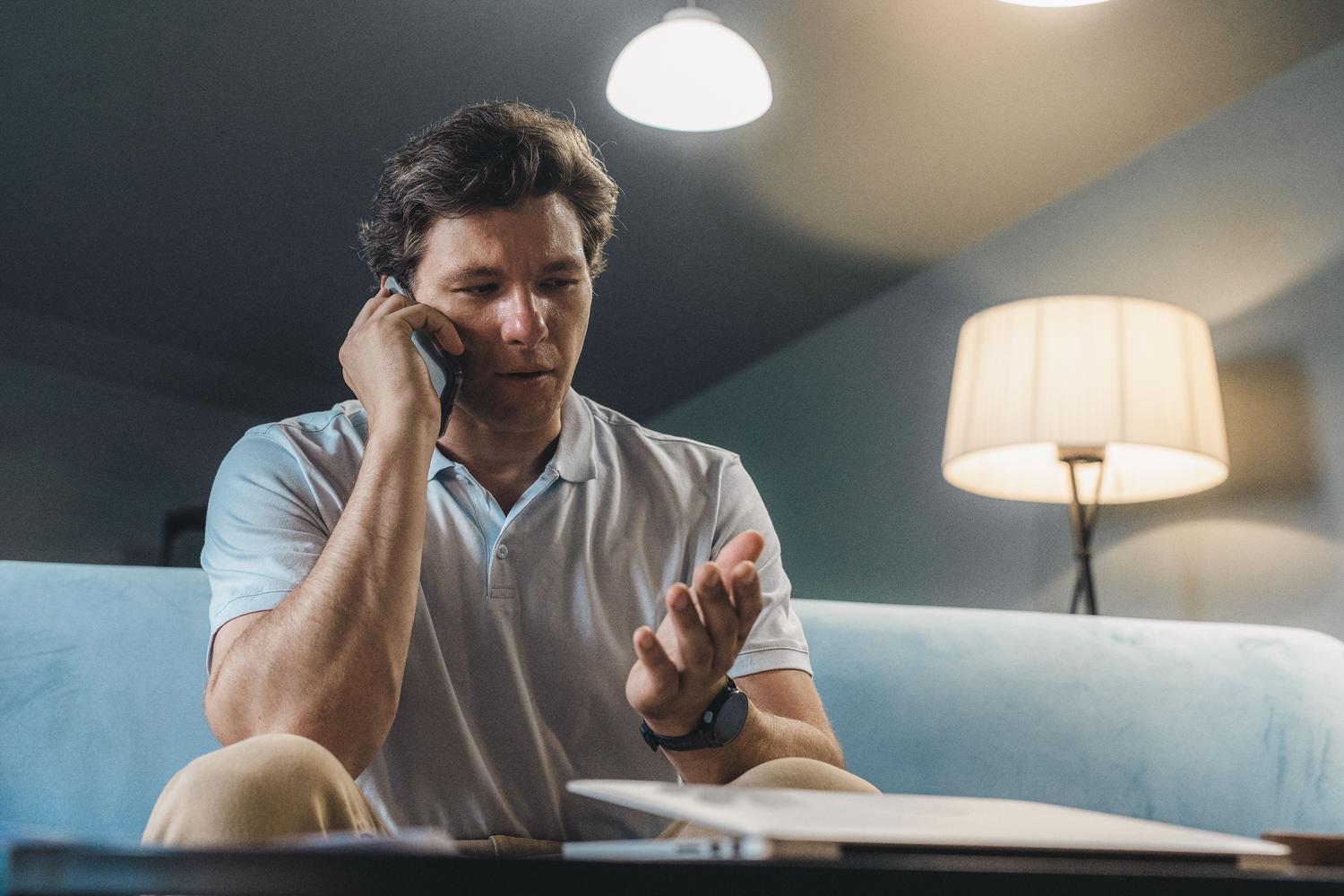 Hombre hablando por teléfono móvil mientras descansa en el sofá de su casa, aprovechando la cobertura Wi-Fi.