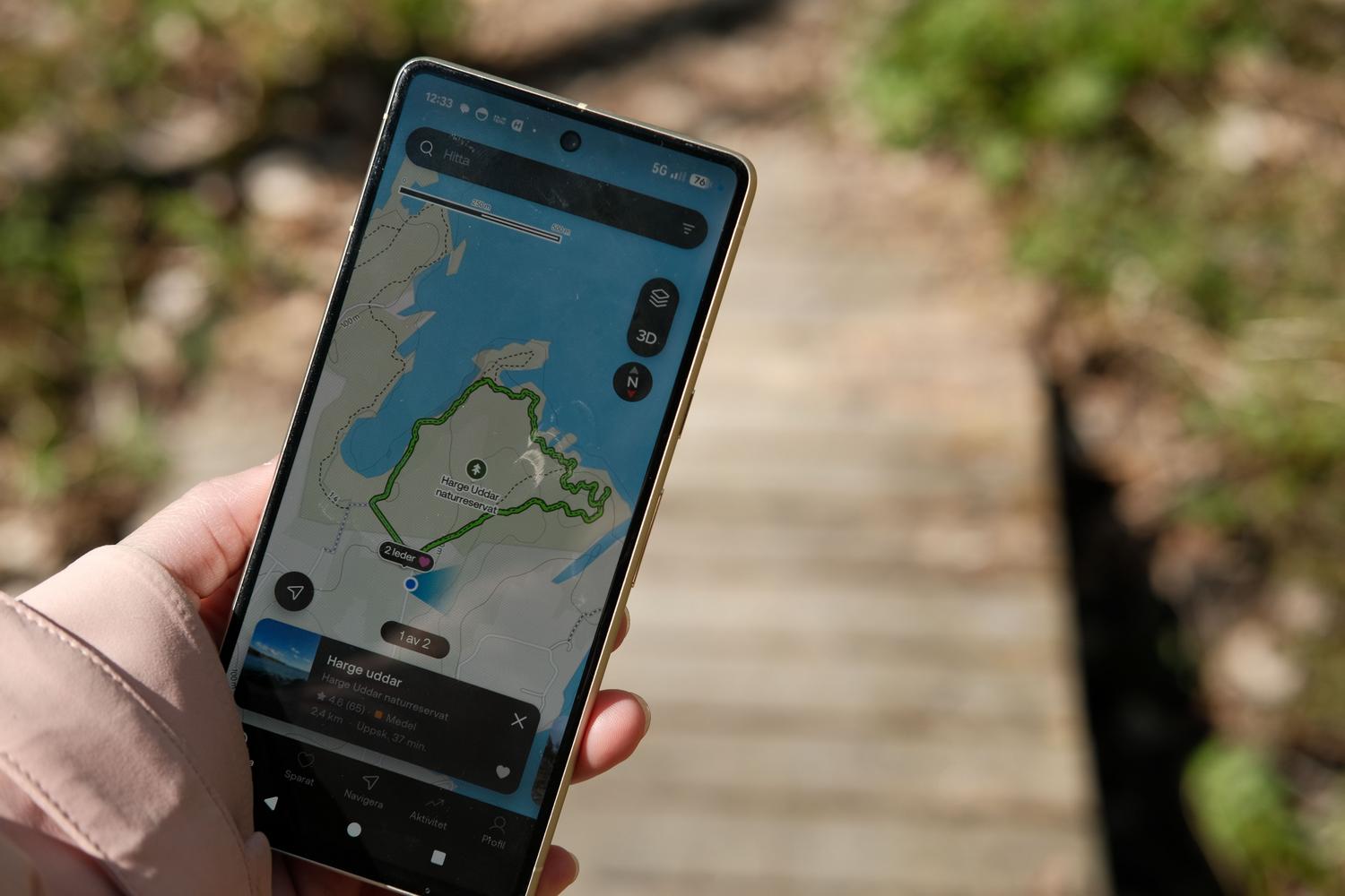 Mano sosteniendo un teléfono móvil con un track GPX y mapa de navegación durante una caminata.