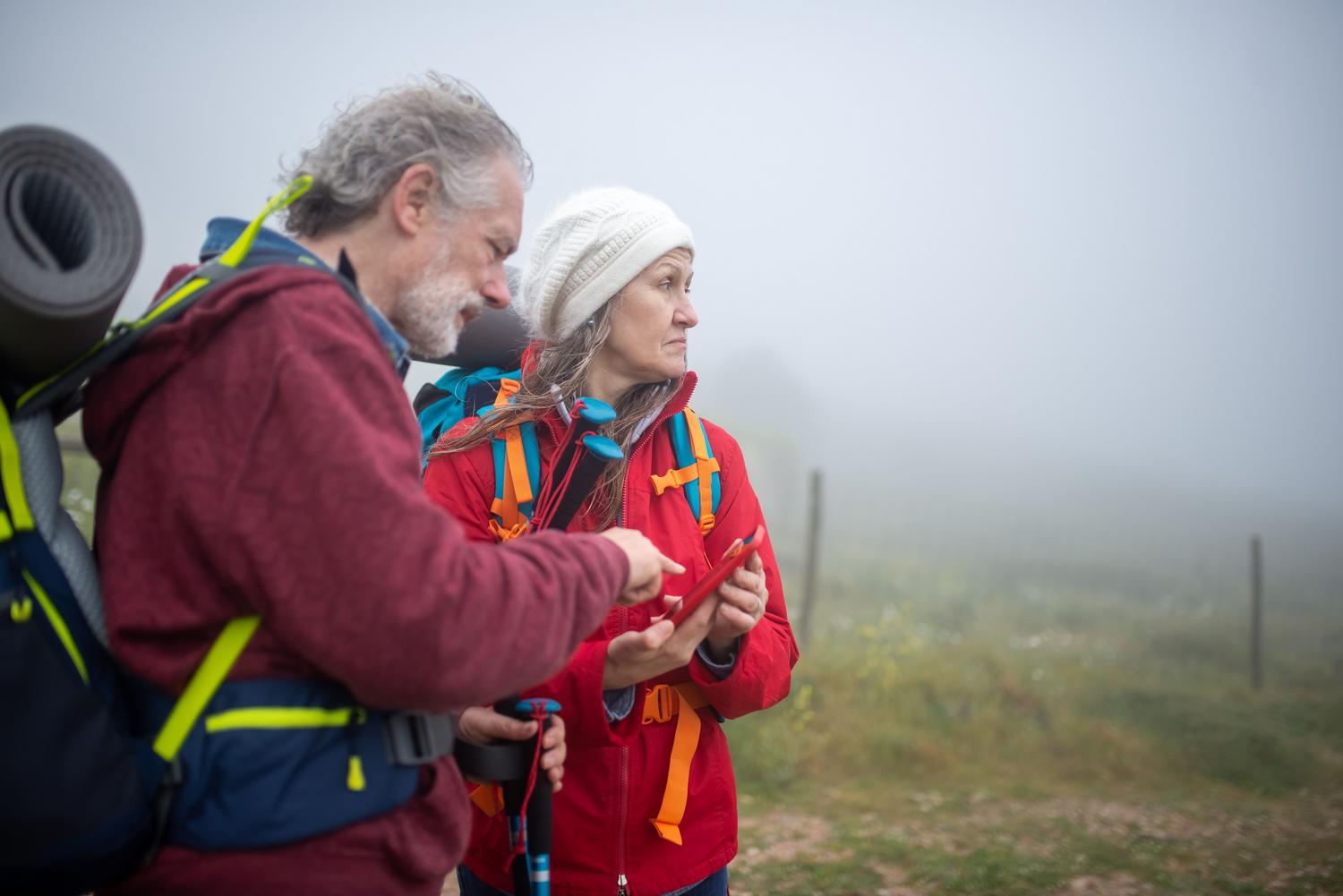 Dos senderistas consultando una aplicación de mapas en un smartphone en un paisaje rural.