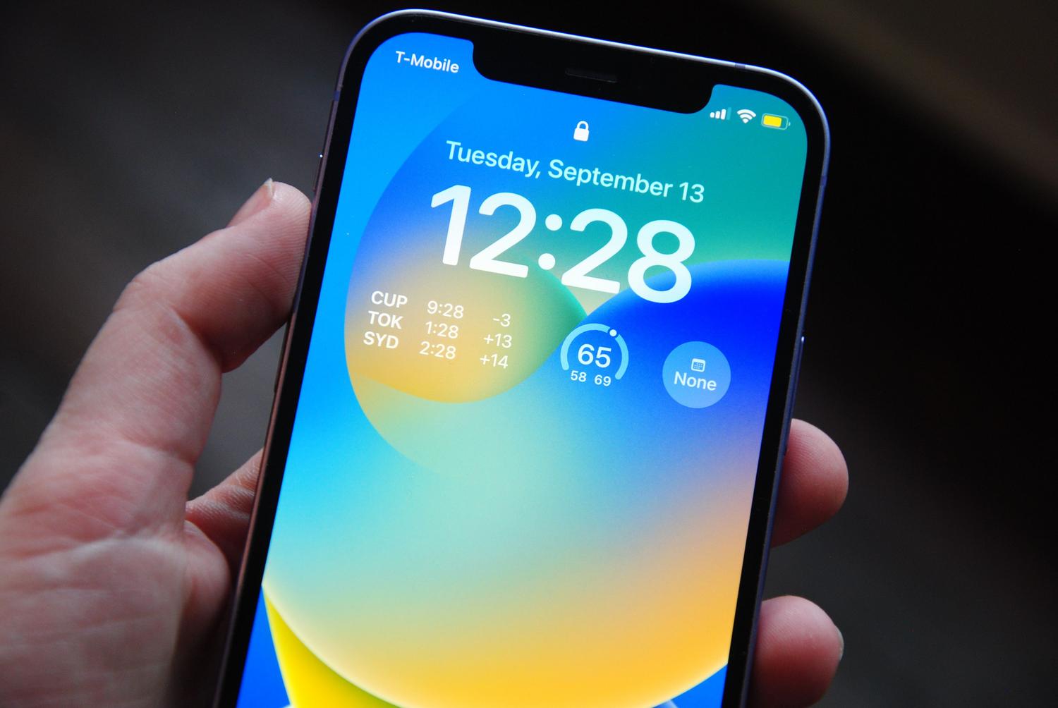 Primer plano de un iPhone moderno mostrando la pantalla de bloqueo con fondos abstractos y widgets.