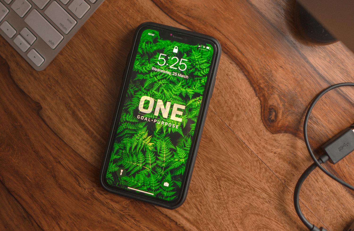 iPhone sobre un escritorio de madera mostrando un texto motivador personalizado en la pantalla de bloqueo.