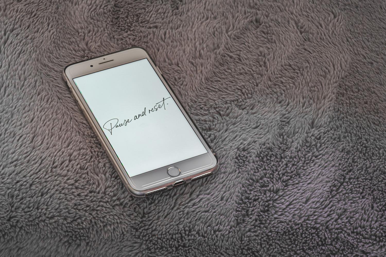 iPhone en un fondo blanco y suave con una frase minimalista de 'Pause and reset' en la pantalla de bloqueo.