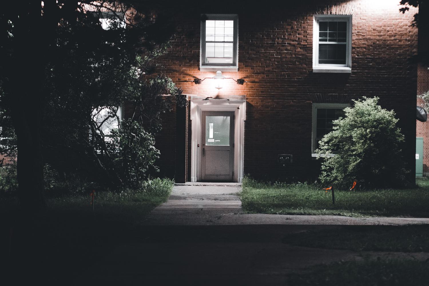 Entrada de una casa de ladrillo cálidamente iluminada durante la noche, creando una sensación de hogar habitado.