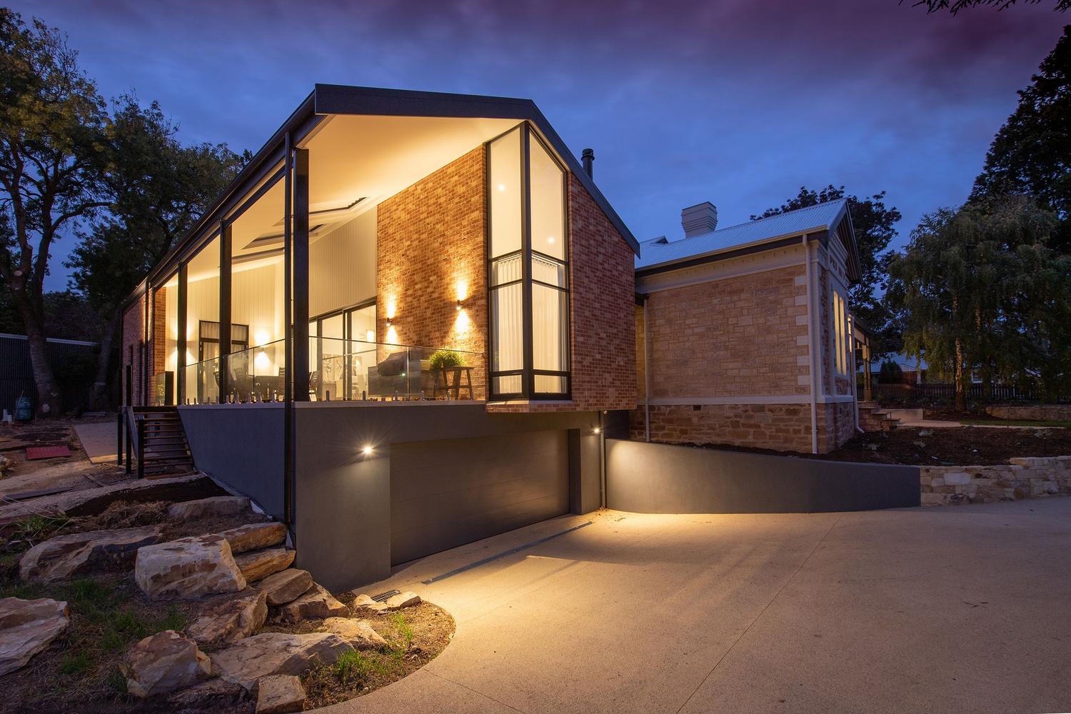 Fachada de una casa moderna iluminada al anochecer, simulando la presencia de habitantes para disuadir robos.