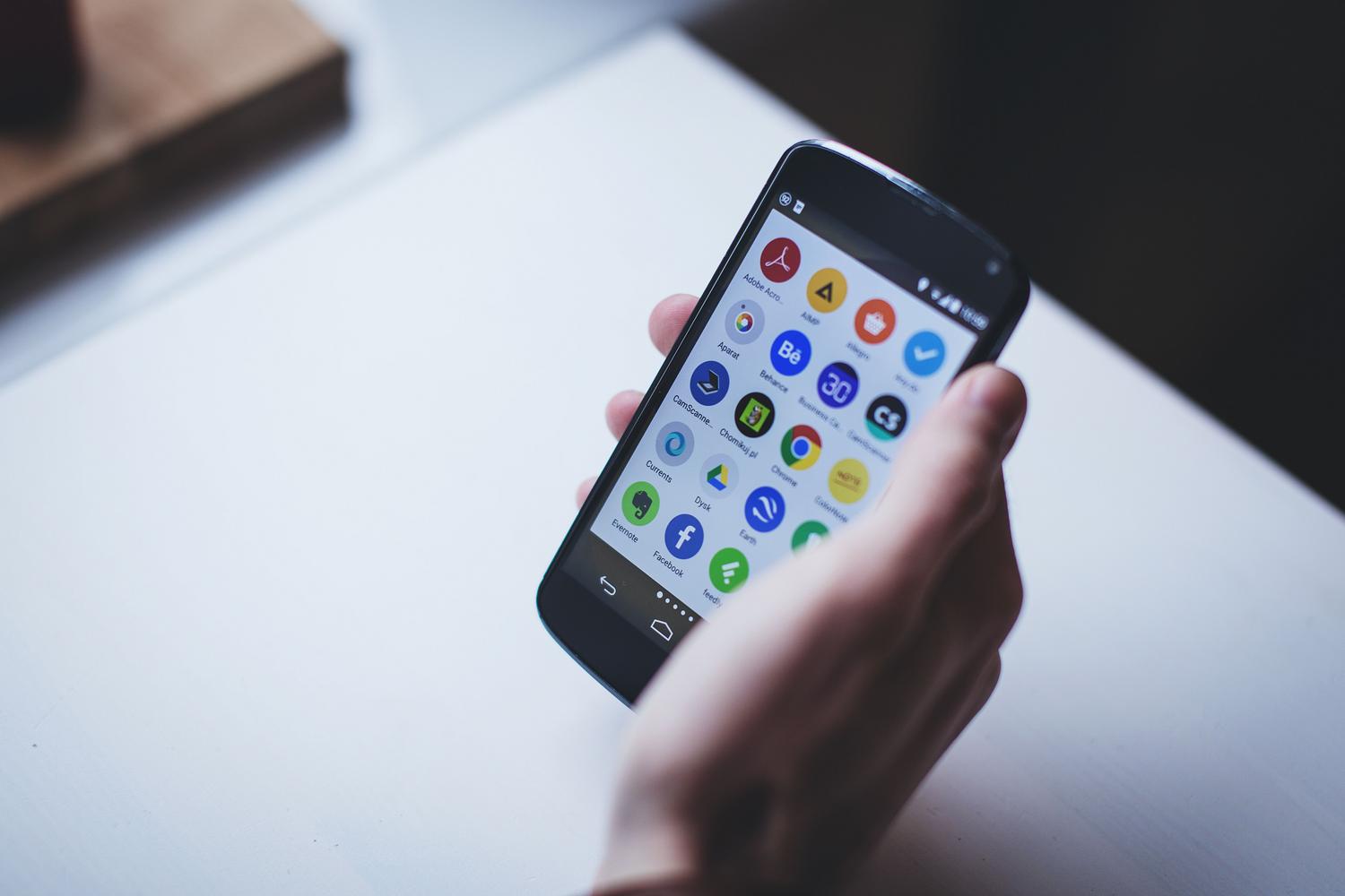 Persona sosteniendo un smartphone Android con una gran variedad de iconos de aplicaciones, representando el amplio ecosistema de software.