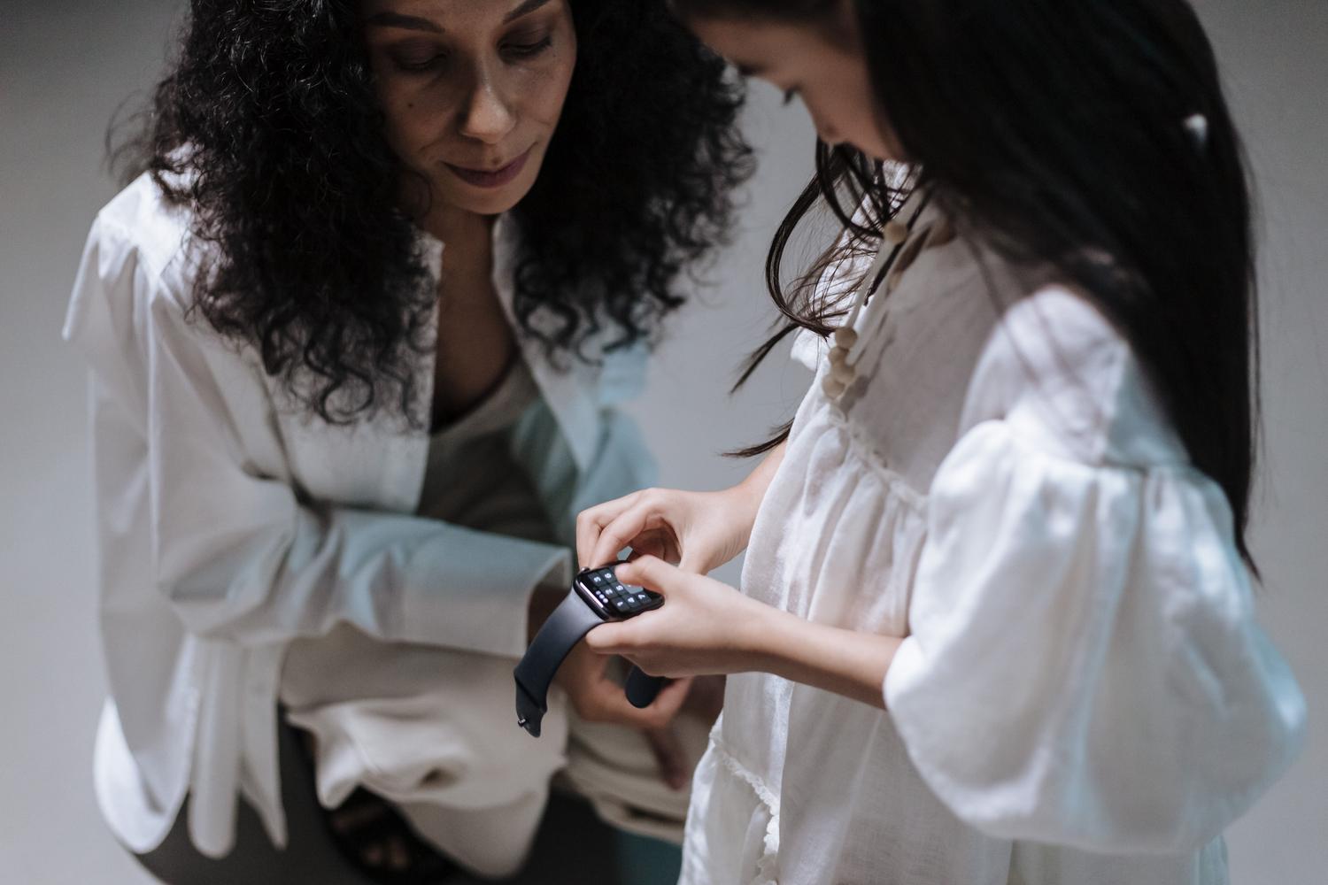 Madre e hija compartiendo un momento mientras revisan un smartwatch, simbolizando el control parental y la complicidad.