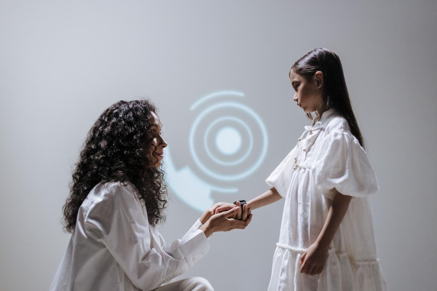 Madre ayudando a su hija a configurar un smartwatch en un entorno minimalista y vanguardista.